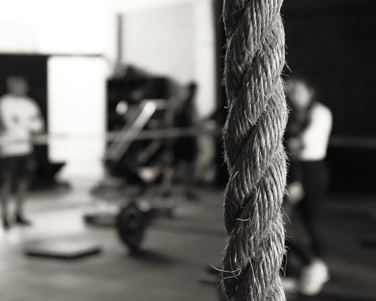 A climbing rope hanging in front of a busy training floor, in black and white