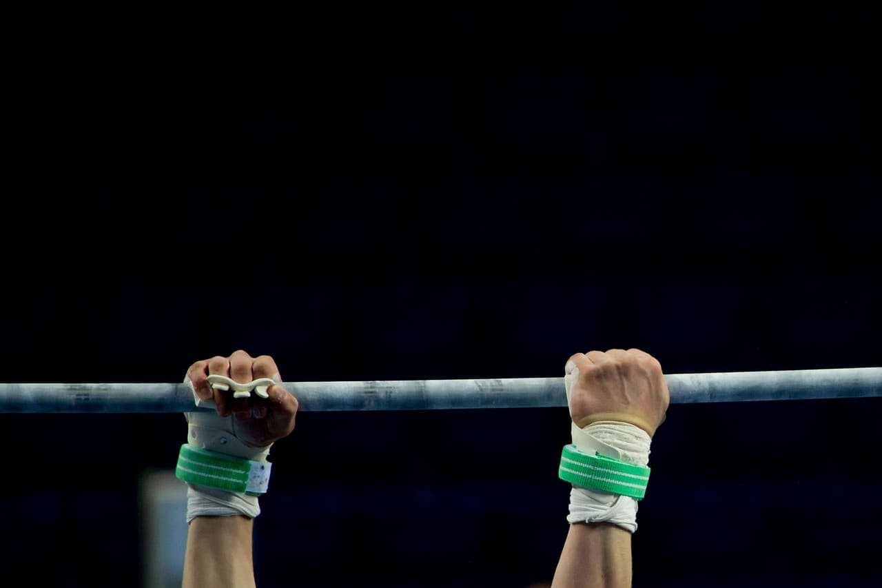 Chalked, taped hands gripping a steel bar against a dark background