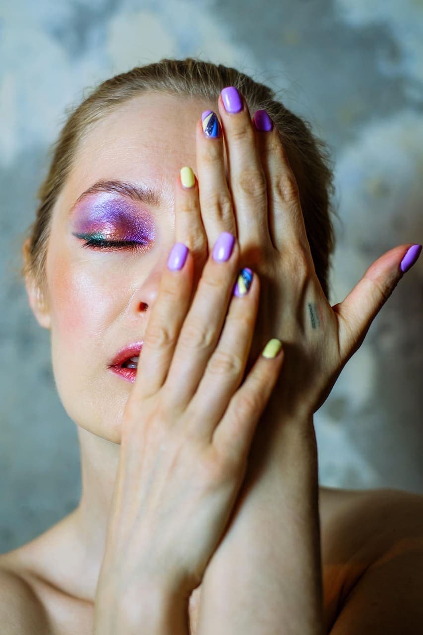 Model covering one eye with a hand painted in a different pastel shade on every nail