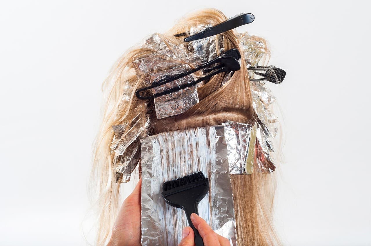 Colourist painting lightener onto lengths between foils