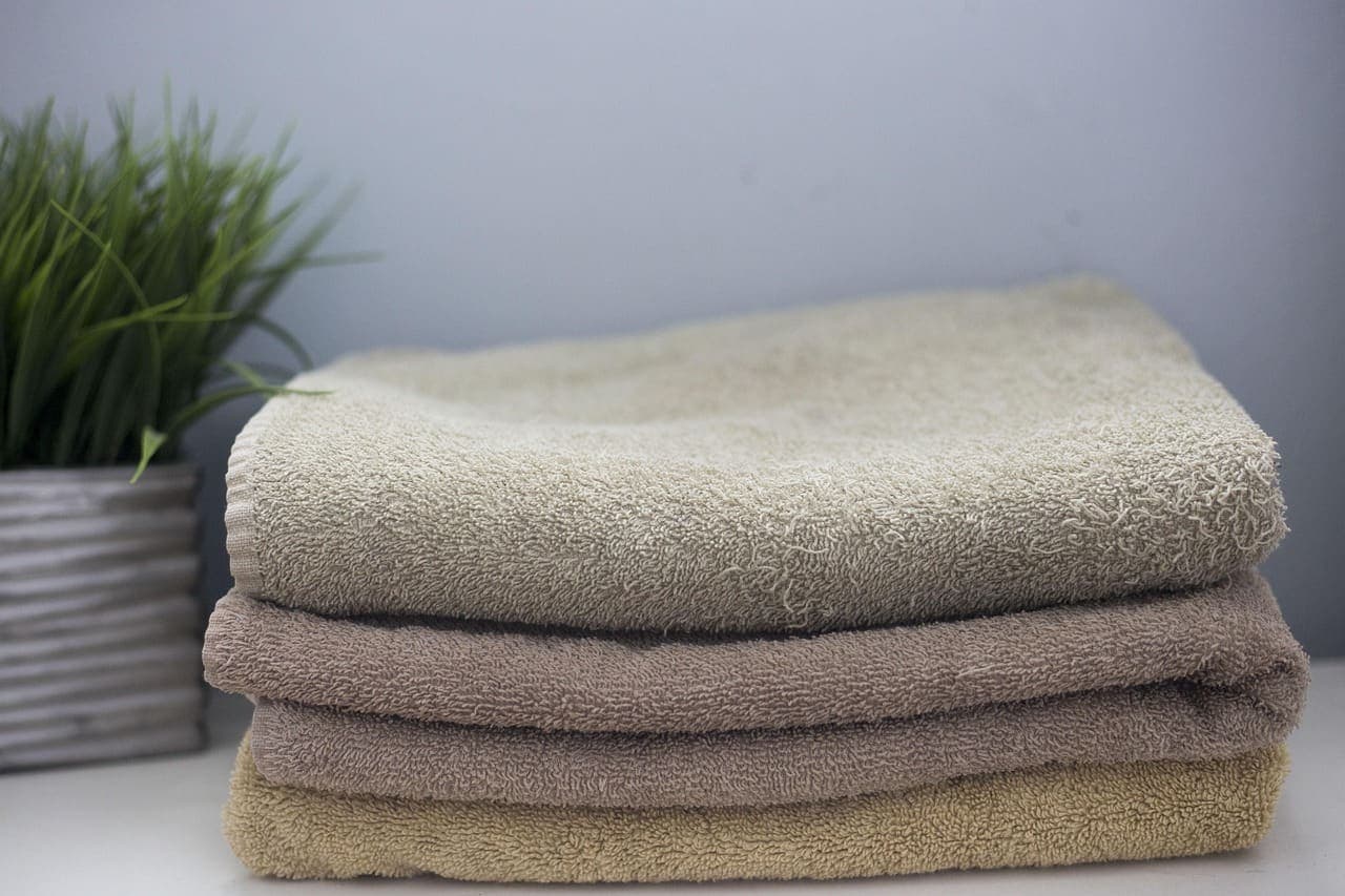 A neat stack of soft sand and stone coloured towels beside a potted grass