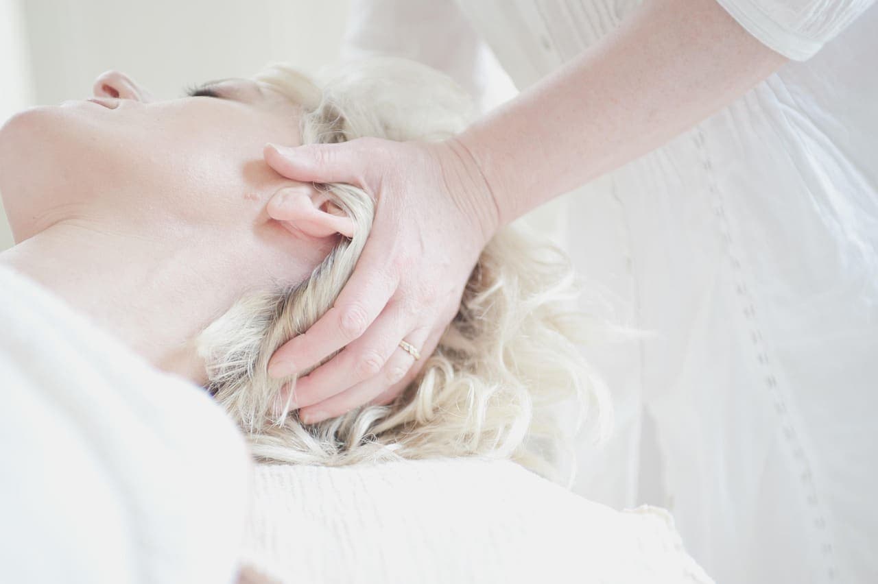 A therapist's hands working slowly through a resting guest's hair in a scalp massage
